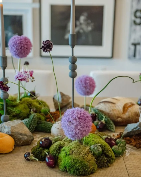 Exquisite floral centerpiece featuring vibrant purple blooms, moss, and decorative stones, enhancing a celebratory table setting for special occasions at XO Bloom.